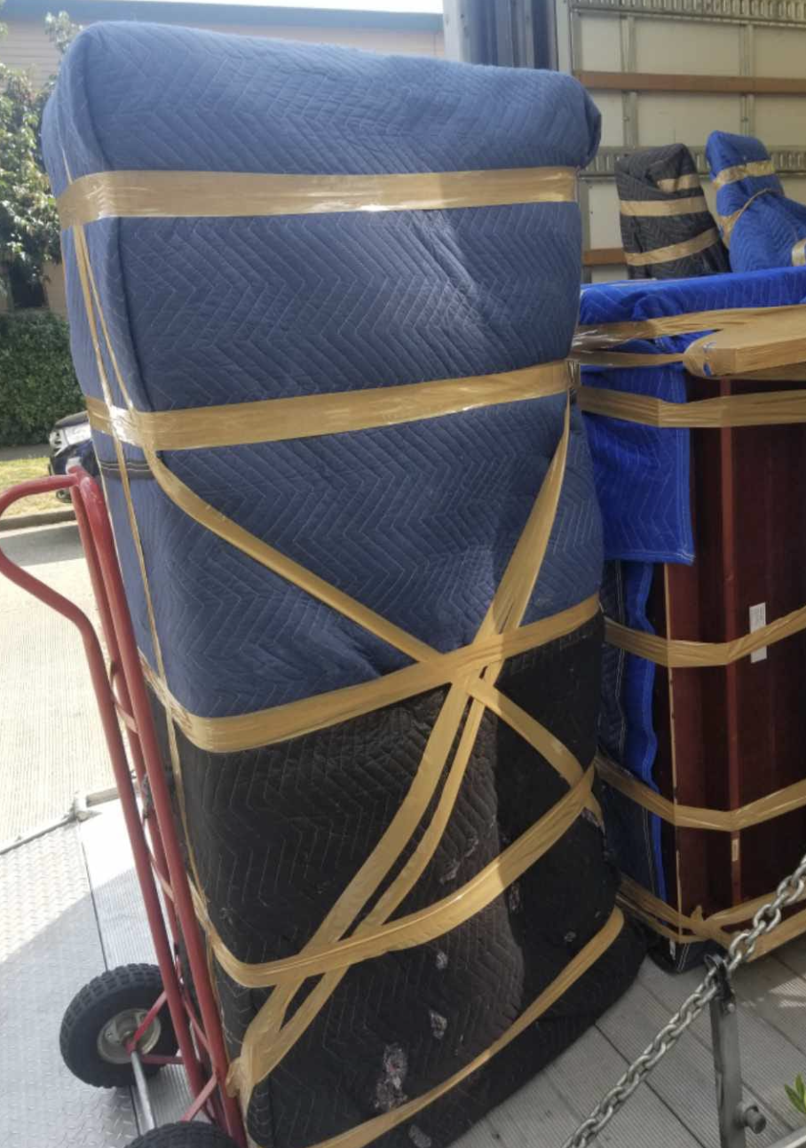Blanket-wrapped furniture strapped to a hand truck at the moving truck ramp