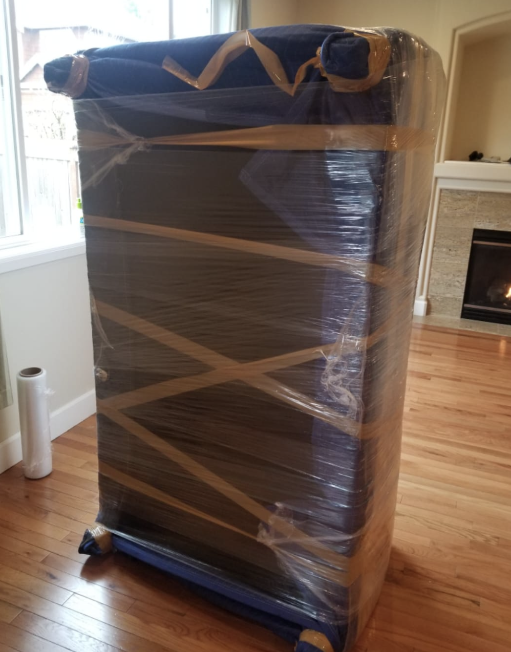 Tall dresser wrapped in moving blankets and shrink wrap inside a home